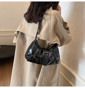 Détail d'un sac porté épaule vintage noir brillant avec boucles argentées sur un trench