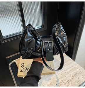 Detail of black glossy faux leather shoulder bag with metallic buckle and retro pleats