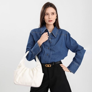 Detail shot of a white pleated dumpling bag held by a model in denim shirt and trousers