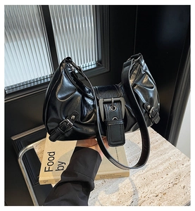Detail of black glossy crescent bag featuring a large metal buckle and smooth leather texture