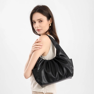 Side view of black pleated cloud shoulder bag worn by model in minimalist studio
