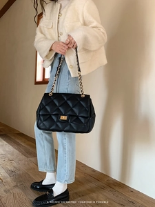 Close-up detail of black quilted texture with golden twist lock on a shoulder bag