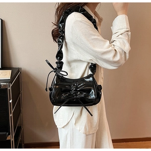 Detail of black glossy faux leather shoulder bag with ruffled strap and bow decoration