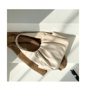 Detail of a creamy white pleated croissant bag on a stone step with sunlight