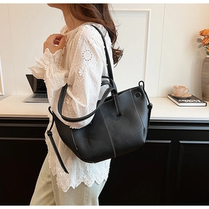 Detail of black pebbled leather tote bag with white contrast stitching and long strap