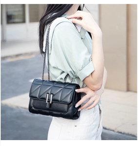 Street style view of a black quilted crossbody bag with a metal chain and flap closure