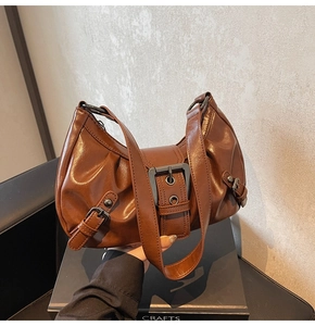 Detail of brown pleated leather handbag showing metallic buckle and wide shoulder strap