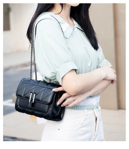 Close-up of quilted black crossbody bag with silver chain strap on a model outfit