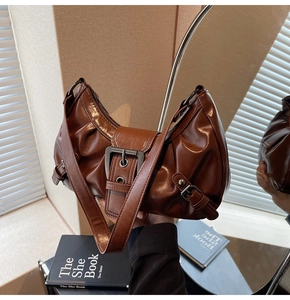 Detail of dark brown glossy leather crescent bag with decorative metallic buckle and straps
