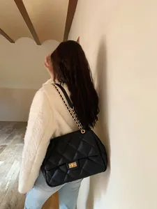 Detailed close-up of a black quilted shoulder bag with gold metal twist lock and chain strap