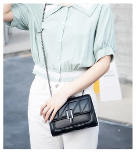Fashionable black quilted crossbody bag with silver buckle worn on mint green outfit