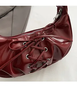 Detail of dark red patent leather handbag featuring cross-strap lacing and silver zipper