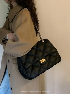 Detail of black quilted chain bag with gold metal rotary lock and crossbody strap