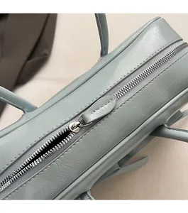 Détail d'une fermeture éclair en métal argenté sur un sac boston bleu clair texturé