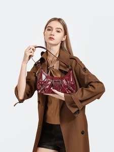 Close-up of a burgundy glossy leather shoulder bag with textured pleats and metal buckles