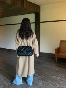 Classic black quilted chain bag detail shown on shoulder in a retro interior setting
