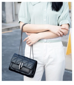 Outdoor street style shot of a quilted black crossbody bag with silver chain strap