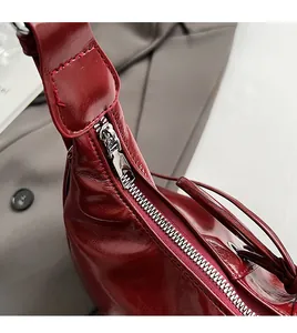 Macro shot of smooth silver metal zipper on a glossy dark red pleated shoulder bag