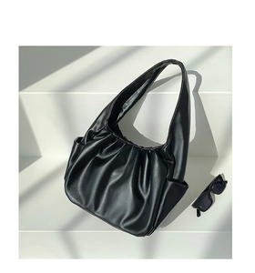 Detail of black pleated croissant bag with matte leather texture on white steps