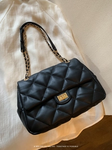 Macro detail of black quilted leather texture and gold chain strap on a shoulder bag