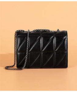 Macro detail of black quilted stitching and gunmetal chain on a structured crossbody bag