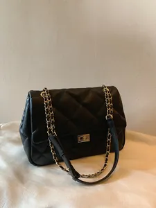 Detail of black quilted leather shoulder bag with gold metal chain and twist lock