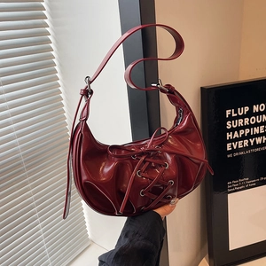 Detail of dark red patent leather hobo bag with corset-style lace-up design and silver eyelets