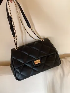 Detail of black quilted leather texture and gold chain strap on classic crossbody bag