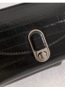 Dettaglio della chiusura ovale d'argento su borsa a tracolla in pelle nera a coccodrillo