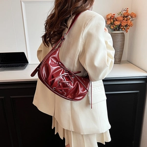Close-up of wine red crescent shoulder bag with lace-up detail and glossy finish