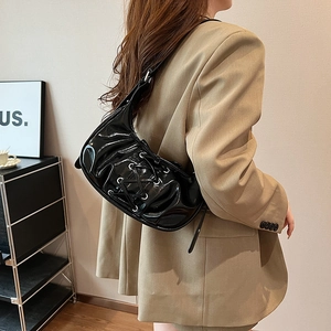 Detailed view of black pleated underarm bag with ballet bow lace-up design on model