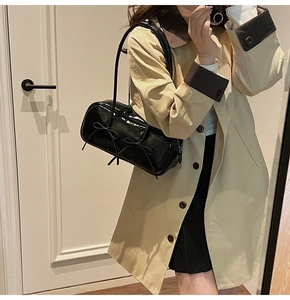Detail of black glossy handbag with bows worn by a model in a beige trench coat
