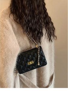 Détail d'un sac matelassé noir avec fermoir tournant doré et bandoulière en chaîne cuir