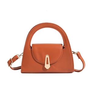 Macro view of caramel trapezoid handbag showing gold geometric buckle and matte leather texture