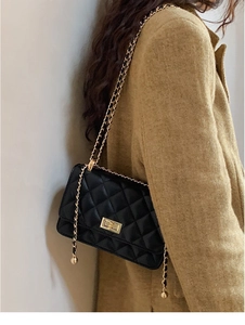 Détail du sac à bandoulière matelassé noir avec chaîne dorée et ornement sphérique