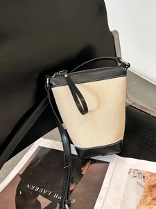 Detail view of canvas bucket bag with black leather trim resting on a black chair
