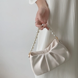 Detail of cream pleated cloud bag featuring elegant large pearl handle and gold metal rings