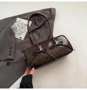 Détail du sac à bandoulière en cuir brillant marron foncé avec des nœuds décoratifs