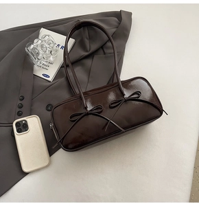 Détail d'un sac à bandoulière en cuir verni marron foncé avec nœuds sur un blazer