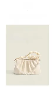 Macro shot of cream-colored pleated cloud bag with large pearl chain and gold hardware