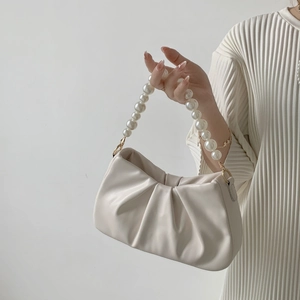 Detail of creamy pleated cloud bag featuring glossy pearl handle and golden hardware