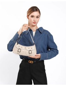 Detail view of a beige textured leather baguette bag with dual buckle front pockets
