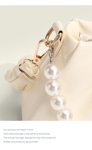 Macro view of cream gathered leather bag with gold hardware and large pearl strap details