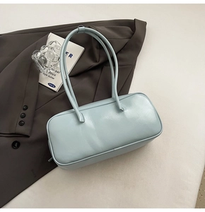 Sac Boston bleu clair posé sur un blazer gris avec des accessoires esthétiques épurés