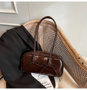 Detail of a brown patent leather bowling bag with vintage bows on a wicker chair