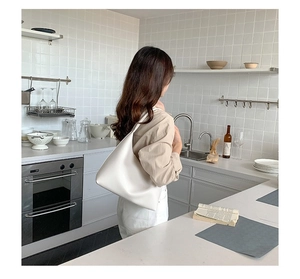 Detailansicht einer weißen minimalistischen Hobo-Tasche, getragen von einem Modell in einer Küche