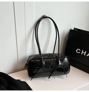 Close-up of black patent leather shoulder bag featuring dual bow accents and silver rivets