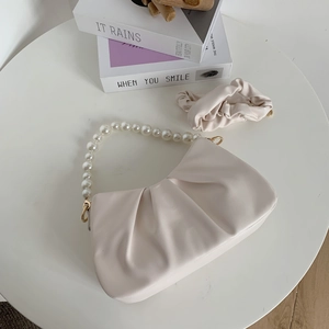 Detail of cream pleated cloud bag with pearl handle and matching scrunchie on table