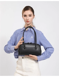Detail of a black leather Boston handbag with stitching and long handles on a model
