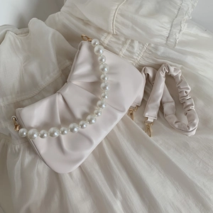 Detail of cream pleated cloud bag with large pearl handle and golden metal hooks